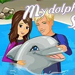 Kaksi henkilöä hymyilee vedessä delfiinin kanssa, taustalla teksti My Dolphin Show 2