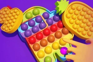 Kuvassa on värikäs pop it -lelu, jossa on eri muotoja ja värejä sekä etualalla lapsen käsi painamassa yksittäistä poppia