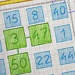 Siniselle ja vihreälle ruudulle kirjoitettuja numeroita ruutupaperitaustalla, yläreunassa tähti